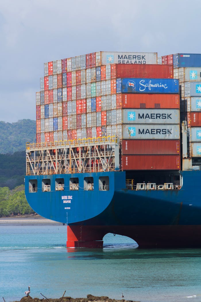 who-we-are A cargo ship loaded with containers navigates the Panama Canal under clear skies.