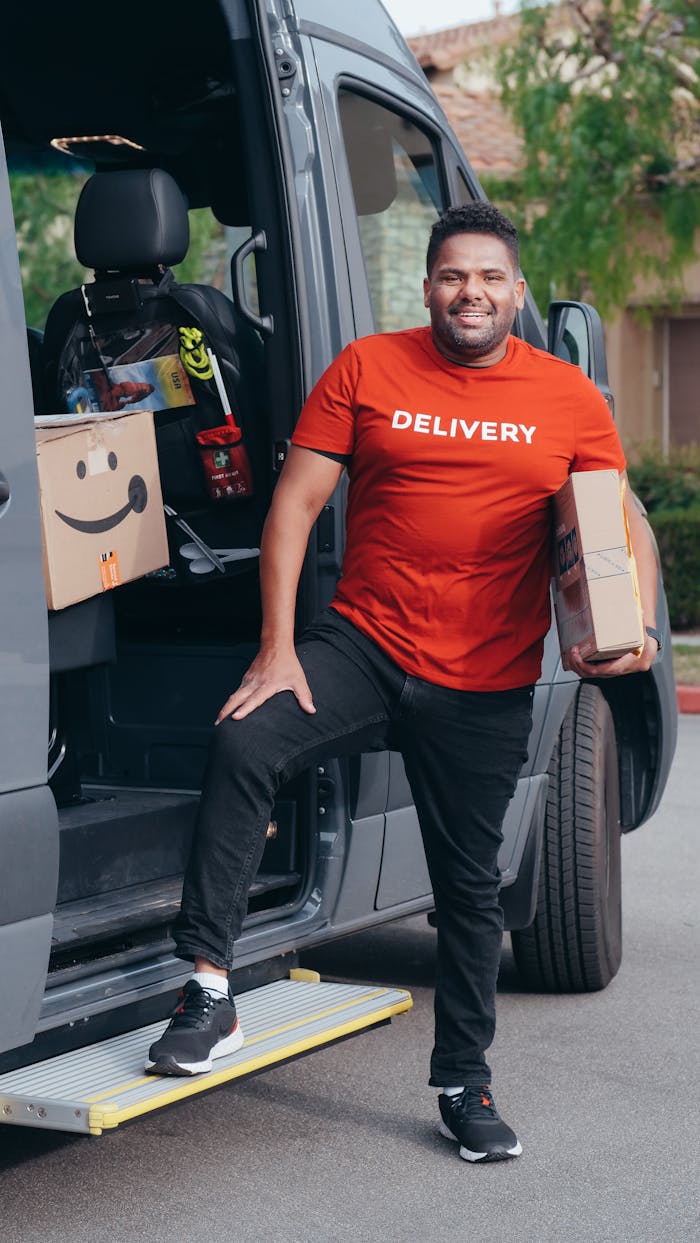 why-choose-us A cheerful delivery man holding parcels next to his van during a workday.